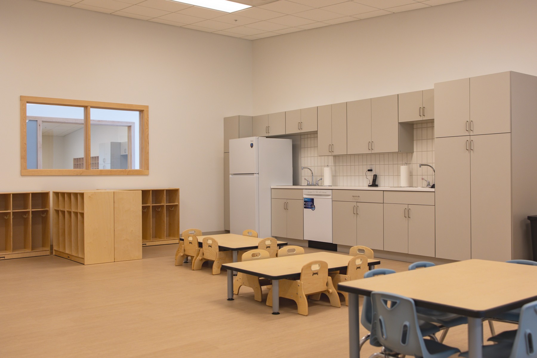 Preschool classroom with small tables, cubbies, and kitchenette